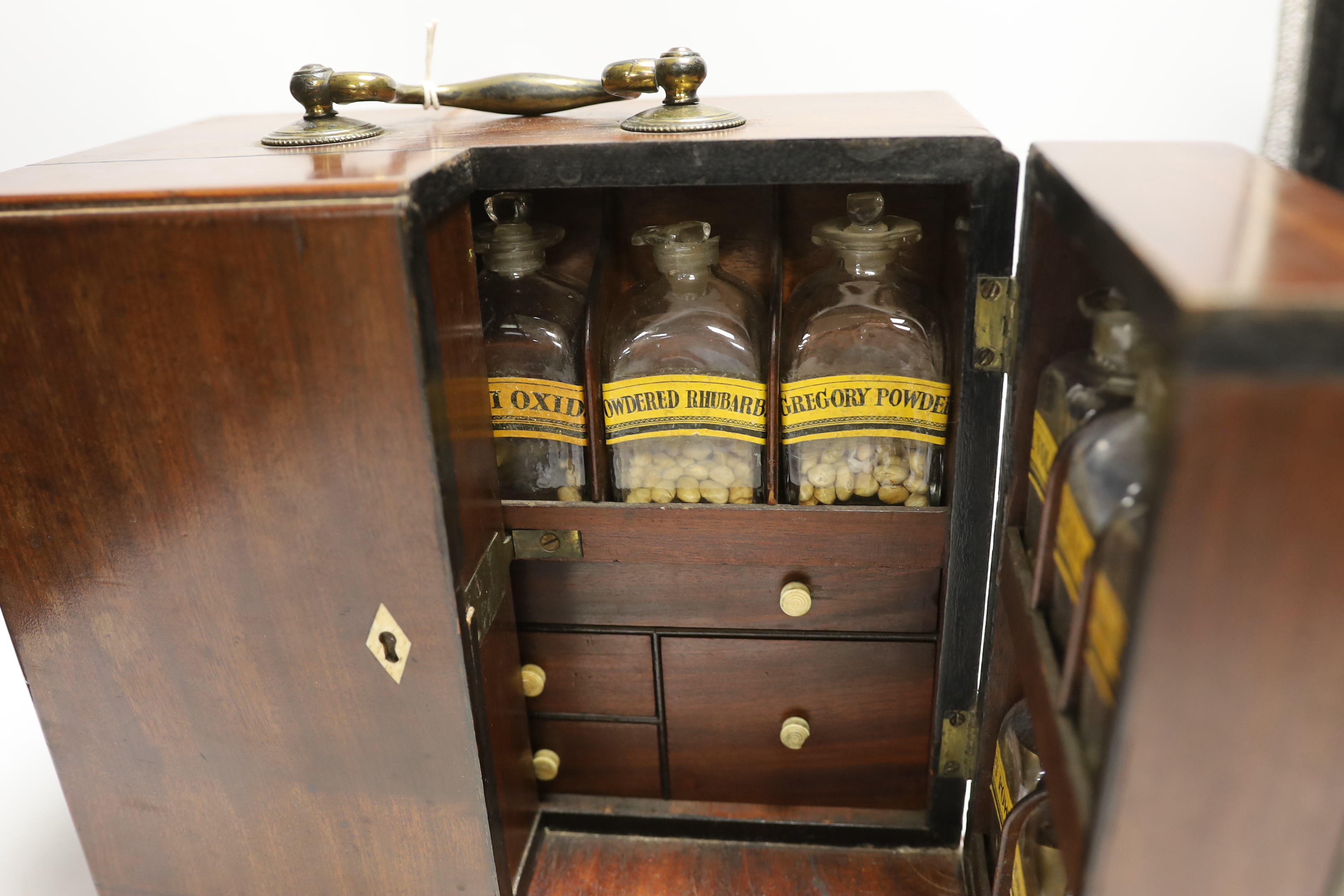 A Georgian mahogany domestic medicine chest, with bone drawer knobs and escutcheons, containing a number of glass square section drug bottles, fitted drawers containing scales, a pestle and mortar, etc., 29cm wide, 25cm